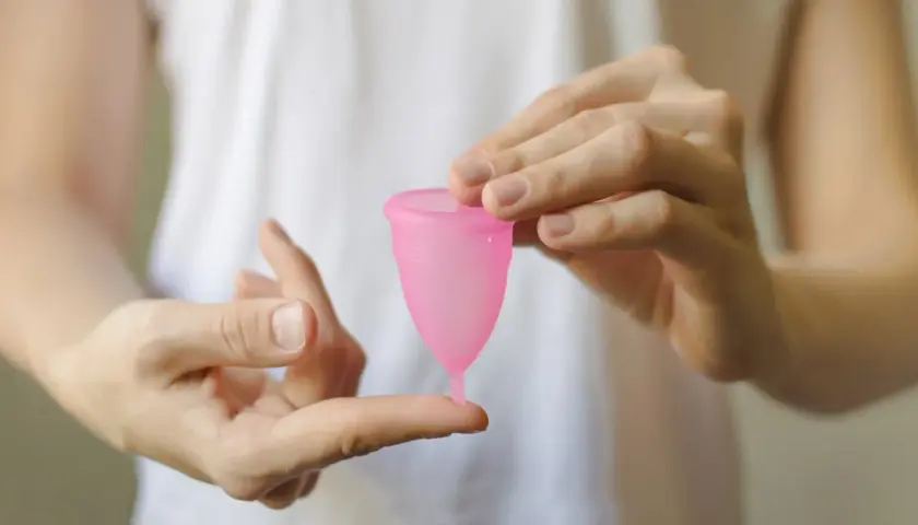 Manos sostienen una copa menstrual rosa. Aprende cómo poner la copa menstrual fácilmente.