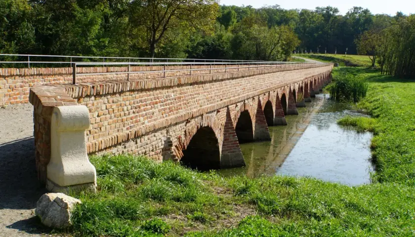 Długi, ceglany most z łukami nad wodą, idealny na trasę rowerową EuroVelo 9.