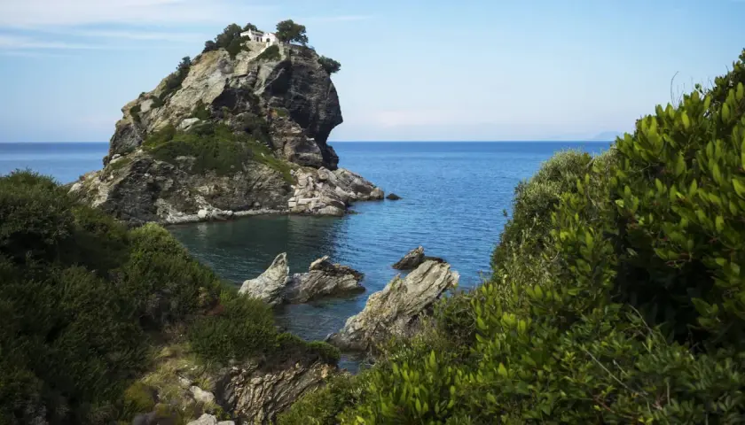 Felsige Klippe mit weißem Haus und Bäumen, umgeben von üppiger Vegetation und dem blauen Meer. Hier wurde Mamma Mia gedreht.