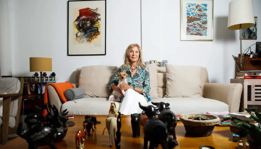 Pilar Eyre, sentada en un sofá con su perro, rodeada de arte y figuras de animales. Un vistazo a su mundo para el blog.