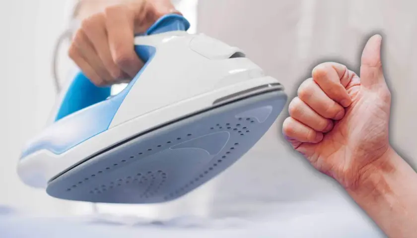 Mano sujetando una plancha blanca y azul, con un pulgar hacia arriba. Aprende como limpiar el suelo de la plancha para un planchado perfecto.