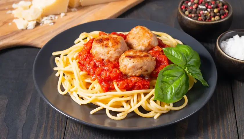 Spaghetti con tres jugosas polpette en salsa de tomate, decorado con albahaca fresca. Un plato clásico y delicioso.