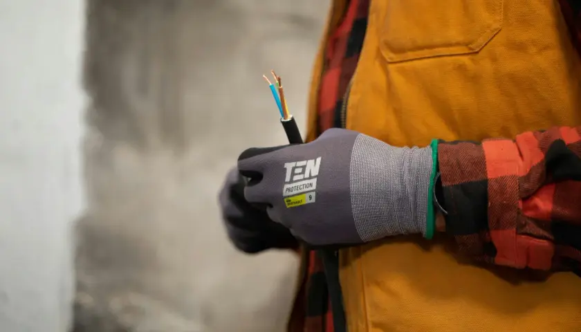 Elektryk w rękawicach ochronnych trzyma kabel elektryczny.