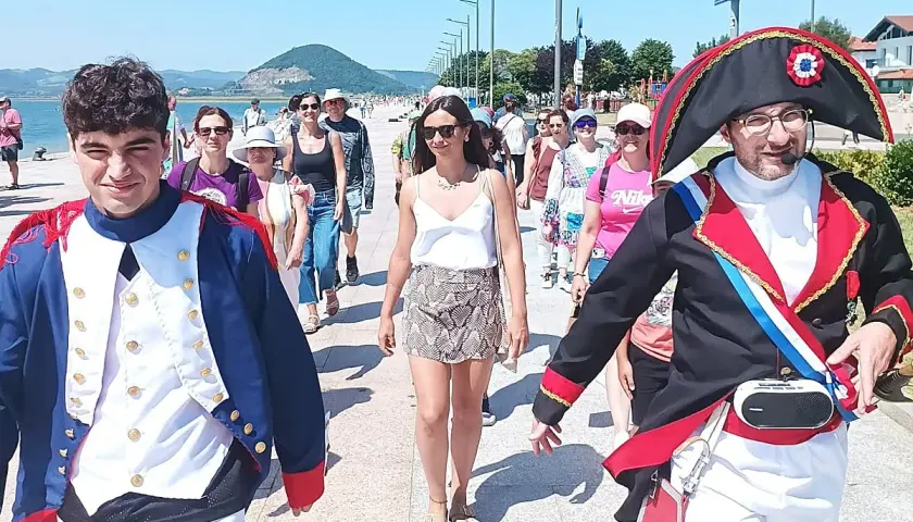 Gente pasea por el paseo marítimo de Santoña, algunos disfrazados, disfrutando del sol y el ambiente festivo.