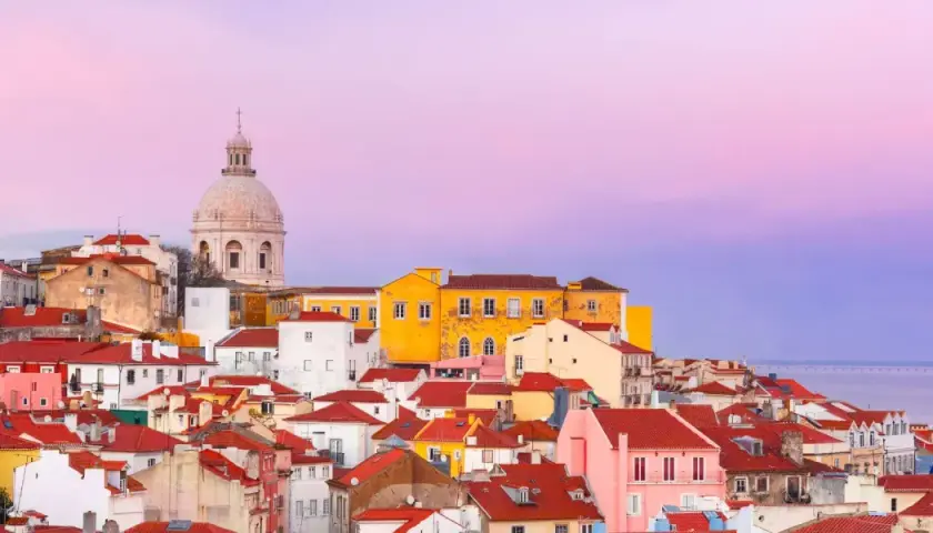 Tejado rojo y cúpula blanca bajo un cielo rosado. Un paisaje urbano que evoca las mejores experiencias en Lisboa.