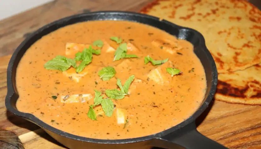 En krämig paneer-rätt i en gjutjärnspanna, garnerad med mynta. Bredvid ligger två gyllene, tunna bröd. Ett perfekt paneer recept!