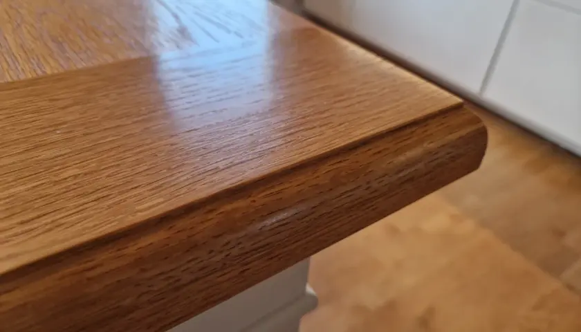 Närbild på ett oljat ekbord med vacker ådring. Bordsskivan har en rundad kant och vilar på en vit bordsstomme.