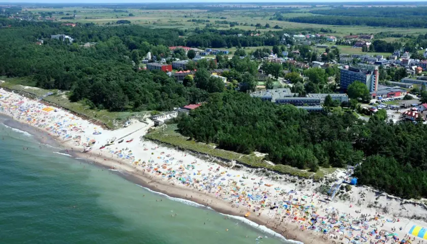 Dąbki: warto jechać! Tłumy ludzi na plaży, zielone lasy i budynki kurortu. Idealne miejsce na wakacje.