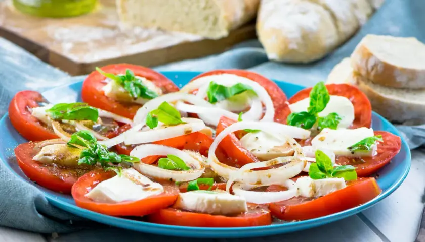 Tomaten-Mozzarella-Salat mit Zwiebelringen und Basilikum, beträufelt mit einem leckeren Dressing. Dazu frisches Brot.