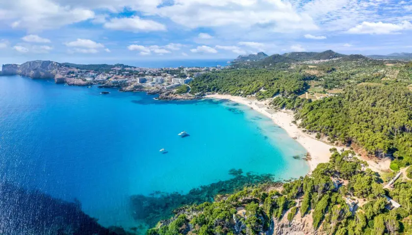 Traumhafter cala ratjada strand mit türkisfarbenem Wasser, weißen Sandstränden und grünen Pinienwäldern. Boote ankern im Meer.