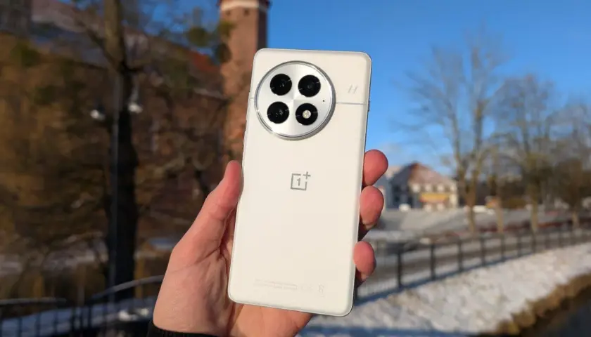 Biały smartfon z charakterystycznym modułem aparatów, trzymany na tle zimowego krajobrazu z zamkiem. System Oxygen OS działa płynnie.