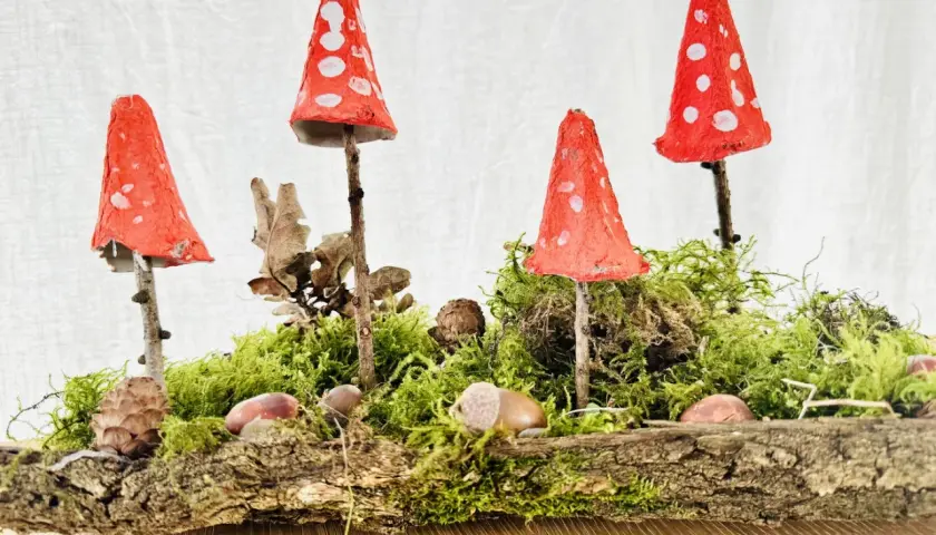 Zauberhafte herbstdeko diy: Fliegenpilze aus Eierkartons auf Moos und Baumrinde, dekoriert mit Zapfen und Kastanien.