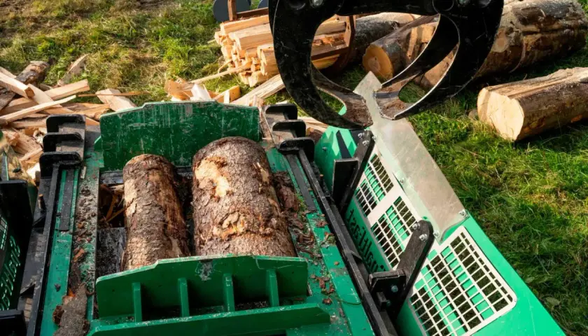 Ein Schichtholzspalter bereitet zwei Baumstämme für die Verarbeitung vor. Ein Greifer hält weitere Holzscheite bereit.