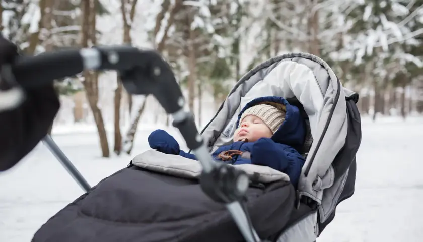 Słodki niemowlak śpi w wózku podczas zimowego spaceru. Otulony ciepłym kombinezonem i czapką, odpoczywa wśród zaśnieżonych drzew.