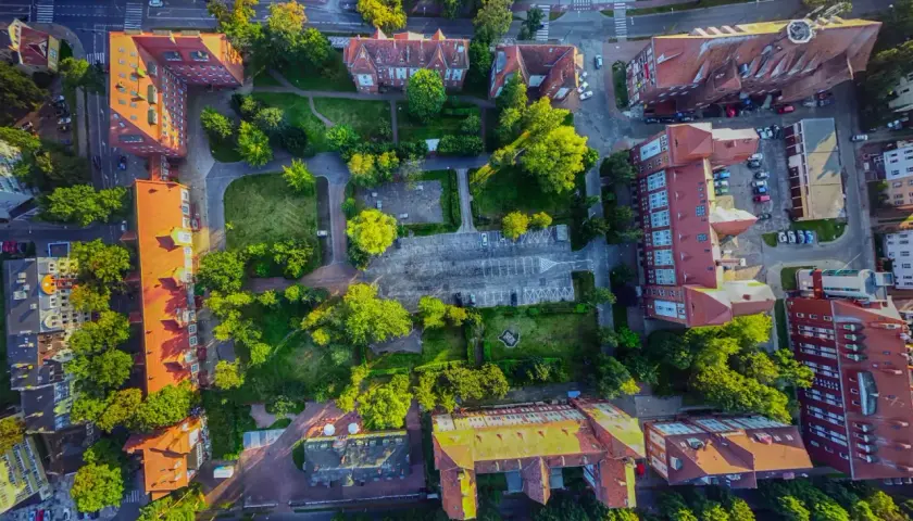 Widok z lotu ptaka na zabudowania i tereny zielone. Widać parking, budynki z czerwonymi dachami i drzewa. Promenada Świnoujście atrakcje w pełnej krasie.