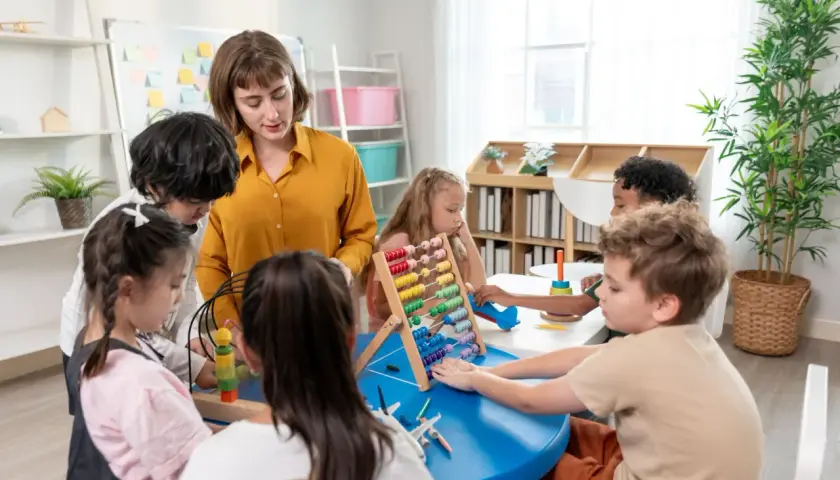 Nauczycielka podczas kursu opiekunki dziecięcej w przedszkolu pomaga dzieciom w zabawie z liczydłem i innymi zabawkami edukacyjnymi.