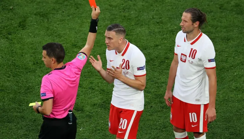 Sędzia pokazuje czerwoną kartkę w piłce nożnej zawodnikowi z numerem 20. Obok stoi jego kolega z drużyny.