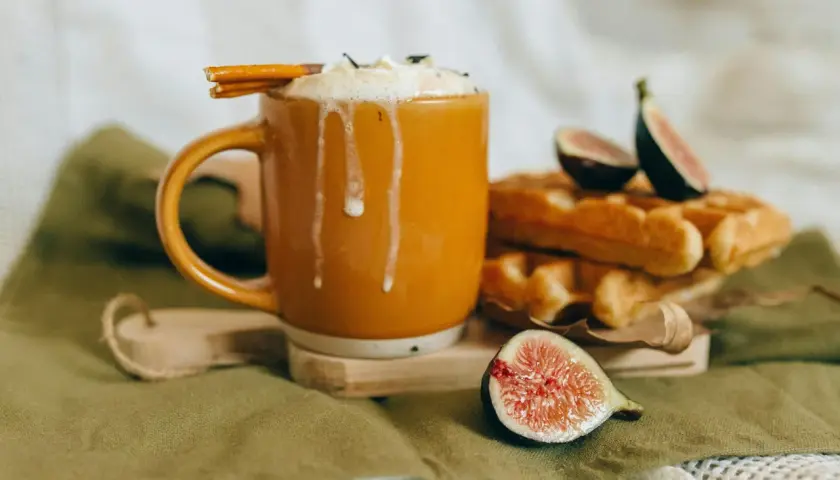 En varm kopp chai latte med vispad grädde och kanelstång, bredvid nybakade våfflor och färska fikon. Perfekt för ett mysigt chai latte recept.