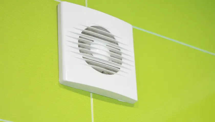 Aspiratore elicoidale o centrifugo bianco montato su una parete verde brillante.