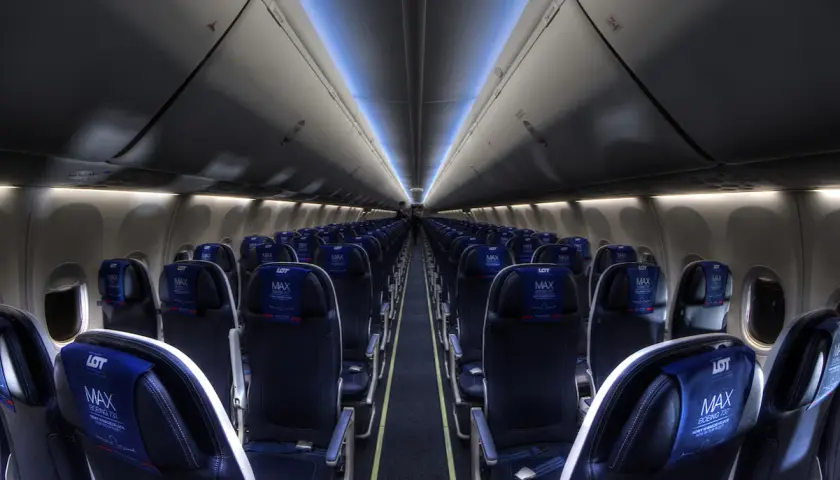 Wnętrze samolotu Boeing 737 MAX 8 LOT, rzędy ciemnych foteli z niebieskimi zagłówkami z logo LOT MAX.