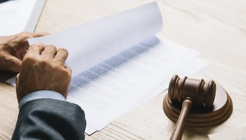 Ręce w garniturze przeglądają dokumenty, obok młotek sędziowski. Może to być akt notarialny gwarantujący dożywotnie zamieszkanie.