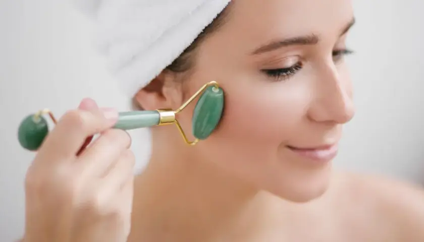 En kvinna med handduk i håret använder en grön jade roller för ansiktet.