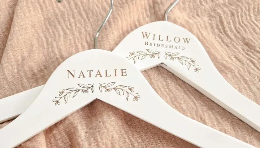 Perchas blancas personalizadas con nombres "Natalie" y "Willow Bridesmaid", adornadas con delicados motivos florales.
