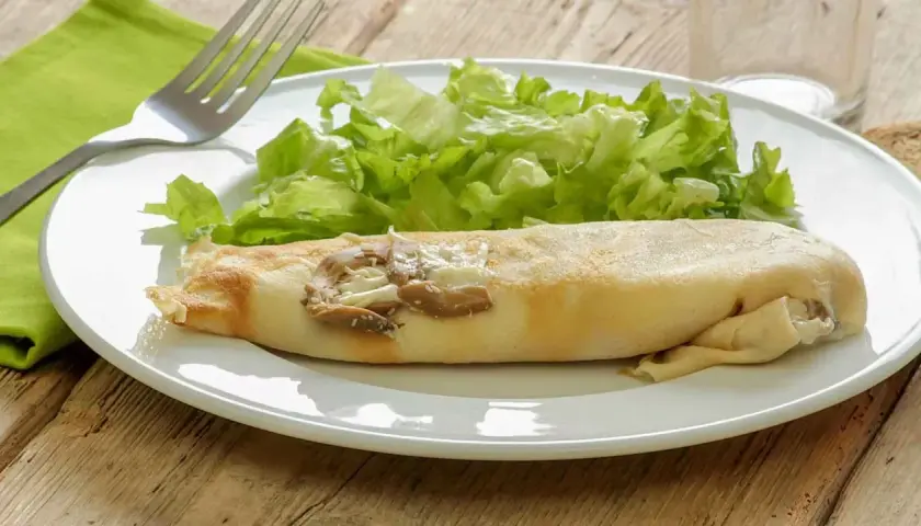 Une ficelle picarde garnie de champignons et de fromage, accompagnée d'une salade verte croquante sur une assiette blanche.