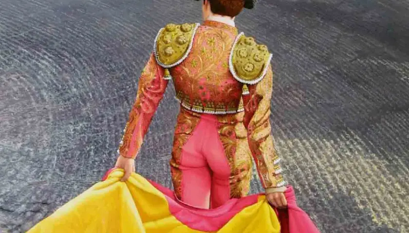 Torero con traje de luces rosa y dorado, sujetando un capote amarillo y rosa. Aprende como hacer un capote de torero.