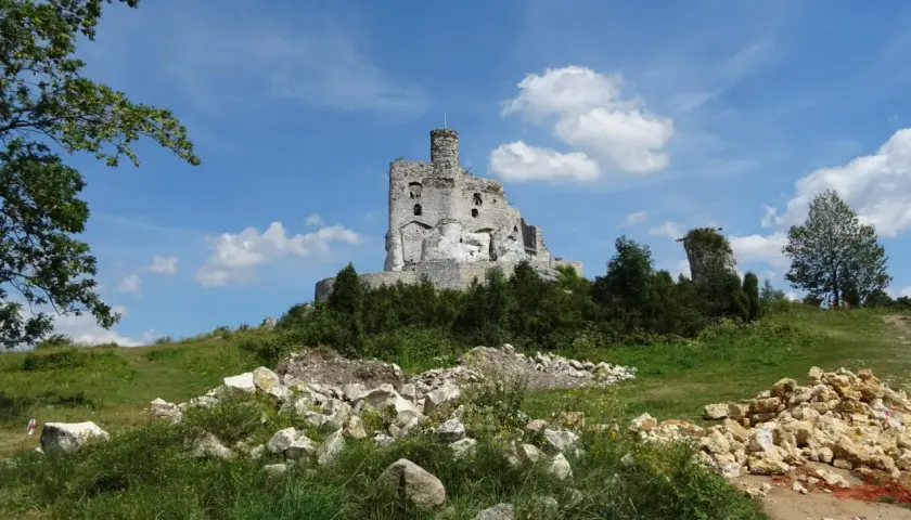 Ruiny zamku Bobolice na wzgórzu, otoczone zielenią i kamieniami.