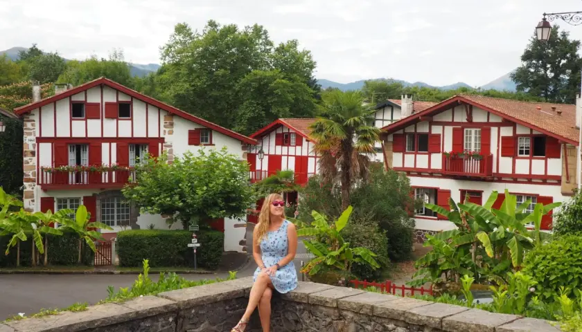 Mujer sentada en un muro de piedra, con casas blancas y rojas típicas del Pirineo Vasco al fondo.