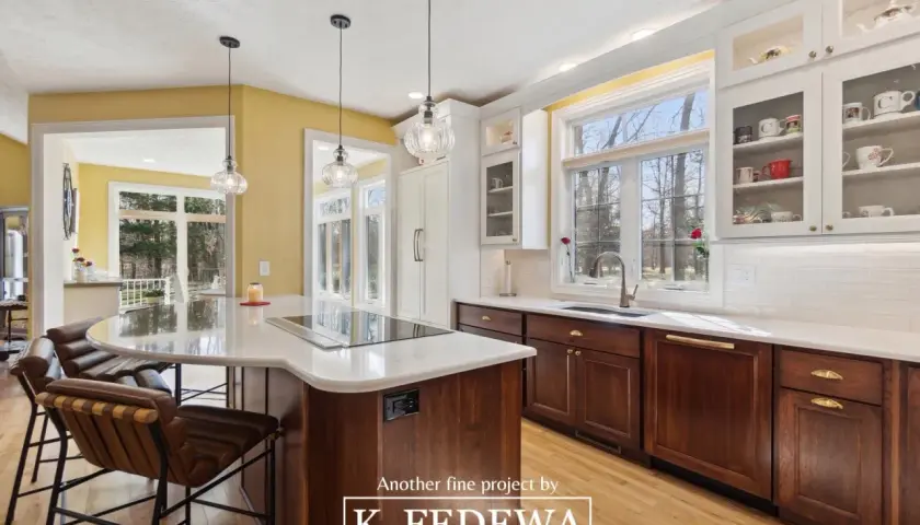 A bright, airy kitchen with natural wood cabinets and a large island. Sunlight streams through large windows, illuminating the warm tones of the wood.