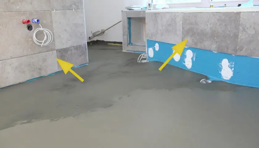 Badezimmer abdichten: blaue Dichtungsbahn und frischer Estrich zeigen den Fortschritt. Gelbe Pfeile markieren wichtige Bereiche.