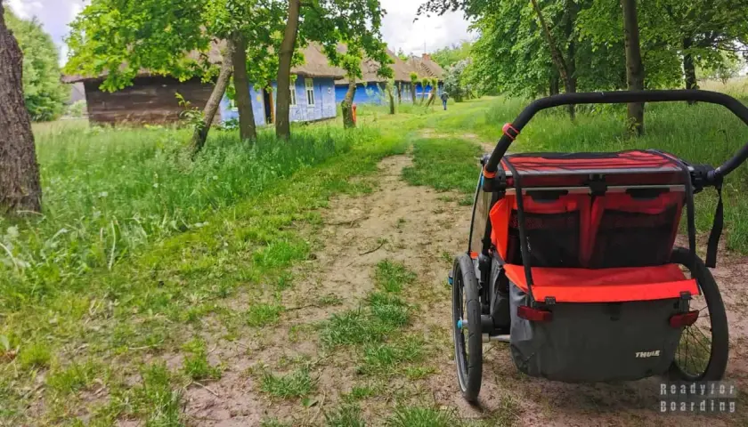 Wózek dziecięcy na tle tradycyjnych, niebieskich chat z krytymi strzechą dachami. Idealne miejsce na wycieczkę, odkrywanie ciekawych miejsc 200 km od Łodzi.