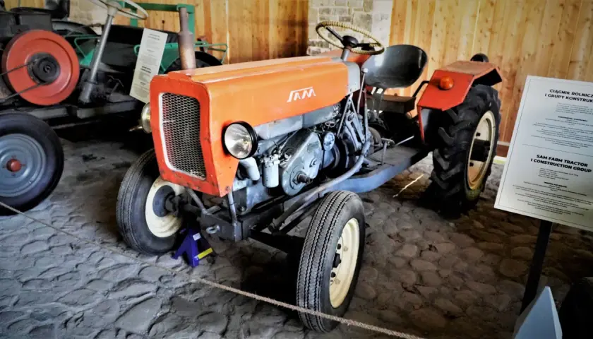 Pomarańczowy traktor SAM, znany jako esiok, z charakterystycznym grillem i silnikiem.