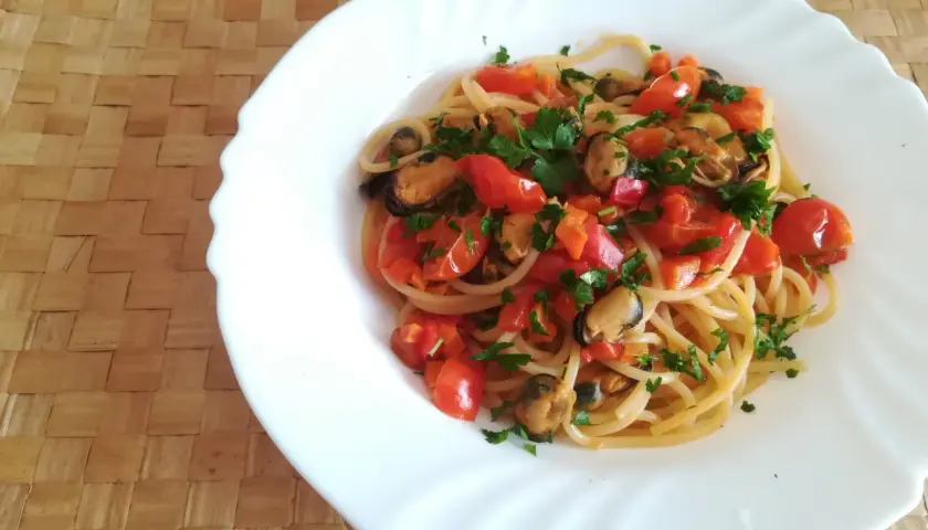 Un piatto di spaghetti con le cozze e pomodorini freschi, guarnito con prezzemolo tritato, pronto per essere gustato.