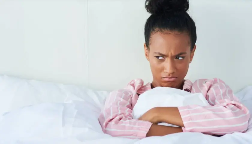 Chica enfadada en la cama, pensando en excusas para no quedar.