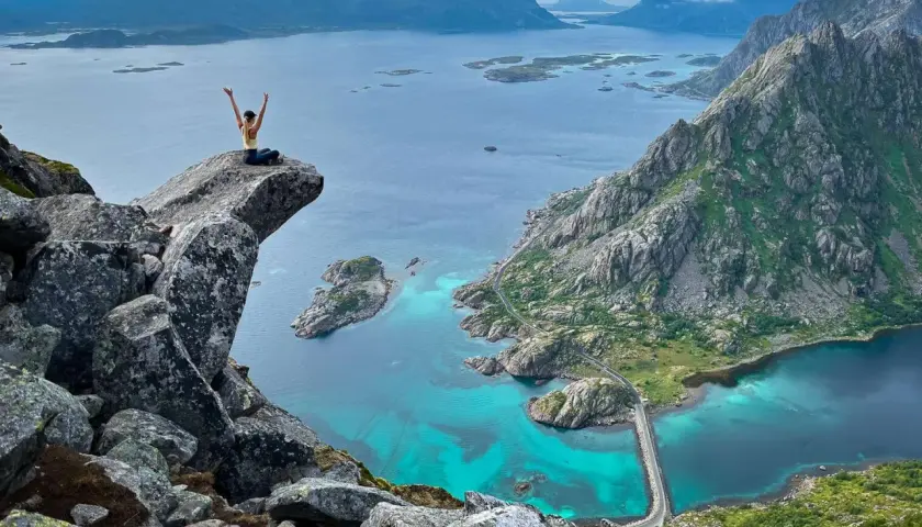 A hiker celebrates on a cliff overlooking turquoise waters and rugged mountains, showcasing some of the best islands for hiking.