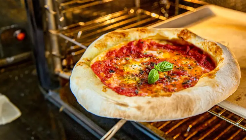 Frisch gebackene pizza vom blech mit geschmolzenem Käse und Basilikum im Ofen.