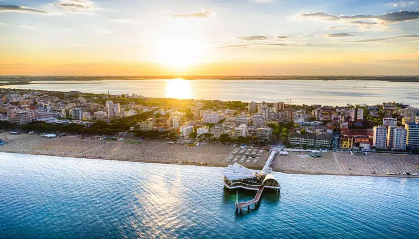 Coucher de soleil sur Lignano, Italie. La plage et la mer s'étendent à perte de vue, avec un pont moderne se jetant dans l'eau.