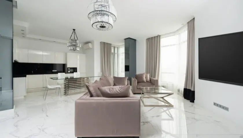 Soggiorno moderno con divani beige, tavolo da caffè in vetro e pavimento in **gres porcellanato cos'è** effetto marmo. Cucina bianca a vista con isola.