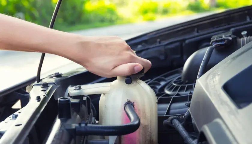 Mano che svita il tappo del serbatoio del liquido refrigerante per la pulizia del radiatore.