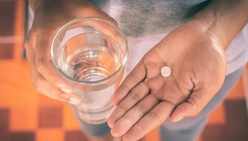Dłoń trzyma szklankę wody i tabletkę, być może Efferalgan Codeine, by złagodzić ból.