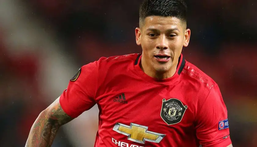 Marcos Rojo w czerwonej koszulce Manchester United, z widocznym logo klubu i sponsora. Jego wiek nie jest widoczny, ale determinacja na twarzy mówi wszystko.