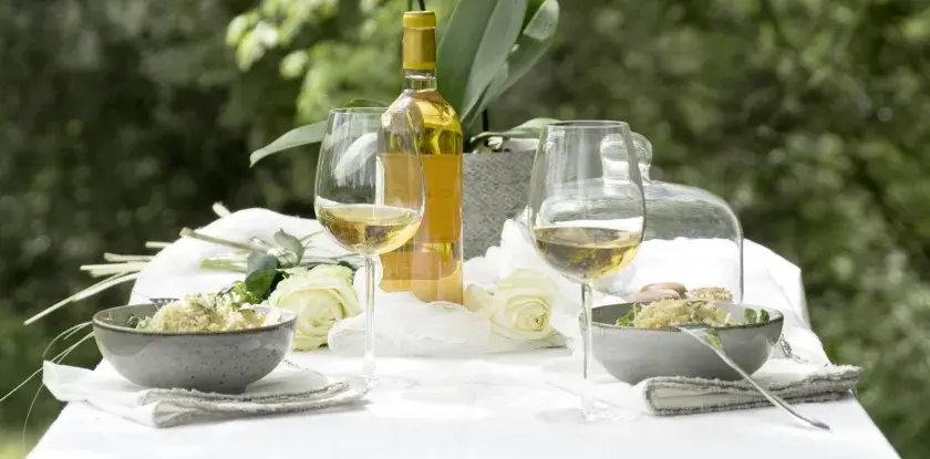 Bordeaux blanc moelleux, deux coupes de vin, deux bols de risotto et des roses blanches sur une table dressée en extérieur.