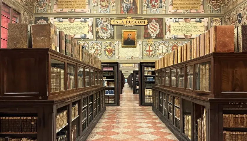 Wnętrze zabytkowej biblioteki z rzędami drewnianych regałów pełnych starych ksiąg, ozdobione malowidłami. To miejsce, gdzie narodziła się nauka, symbolizujące najstarszy uniwersytet na świecie.