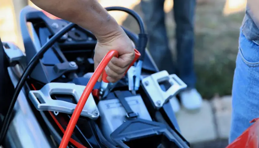 Mano conectando pinza roja para cargar bateria moto.