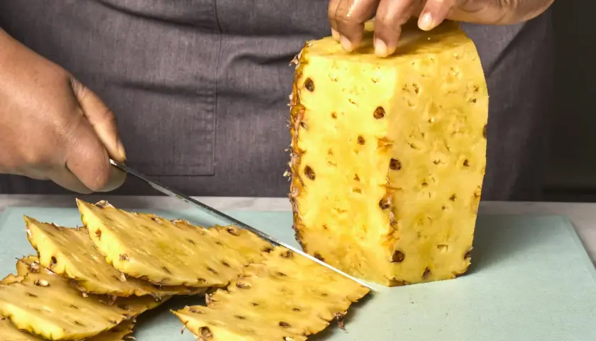Hände schneiden eine Ananas. Dunkle Flecken auf der Frucht könnten ein Hinweis sein, um Ananas Schimmel zu erkennen.