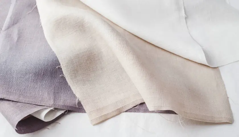 Trois tissus en lin, l'un violet, l'autre beige et le dernier blanc, prêts à blanchir le linge pour un éclat parfait.