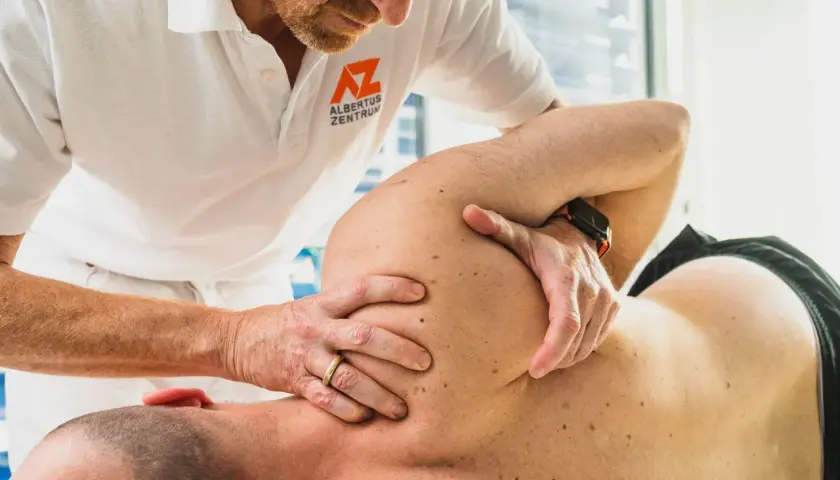 Osteopath behandelt Schulterschmerzen. Hände des Therapeuten am Schulterblatt eines Patienten.